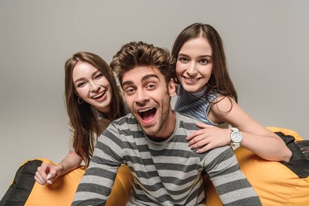 excited friends sitting on bin bag chair together, isolated on grey