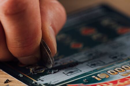 close up view of silver coin in hand of gambler scratching lottery ticketの写真素材