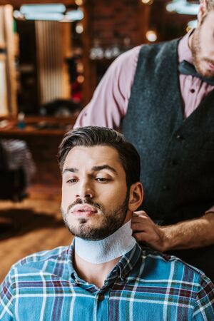 barber fixing collar around neck of handsome bearded manの写真素材