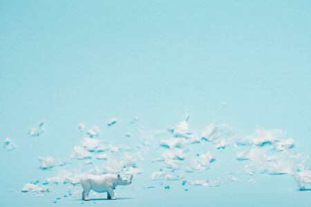 White rhinoceros toy and plastic garbage on blue background, environmental pollution concept