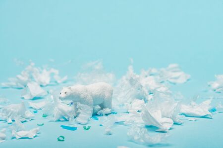 White toy polar bear with plastic garbage on blue background, animal welfare conceptの写真素材