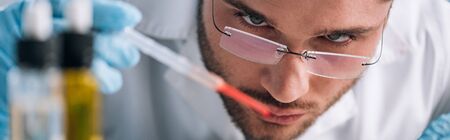 panoramic shot of immunologist holding pipette with red liquid