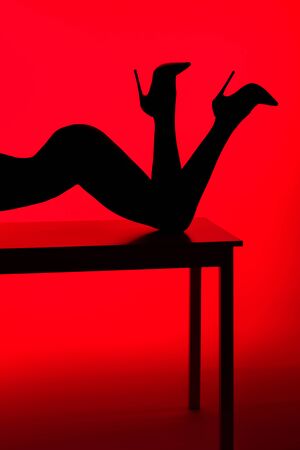 black silhouette of passionate girl in heels posing on table isolated on redの写真素材