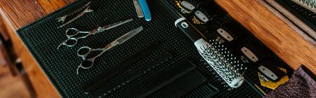 panoramic shot of sharp scissors near hair brush in barbershop