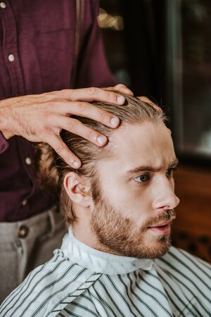 handsome bearded man sitting in barbershop near barberの写真素材
