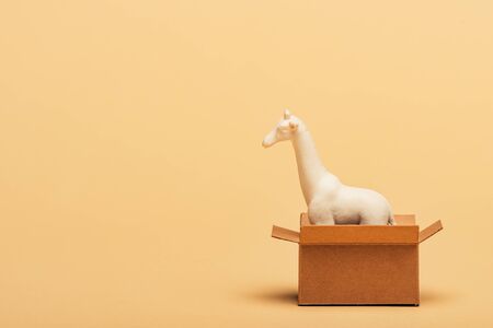 White toy giraffe in cardboard box on yellow background, animal welfare conceptの写真素材
