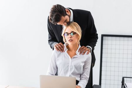 Businessman kissing colleague with laptop in officeの写真素材