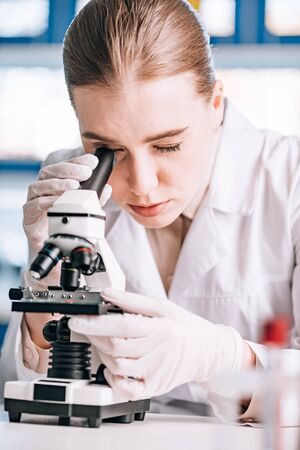 selective focus of immunologist in latex gloves looking through microscope