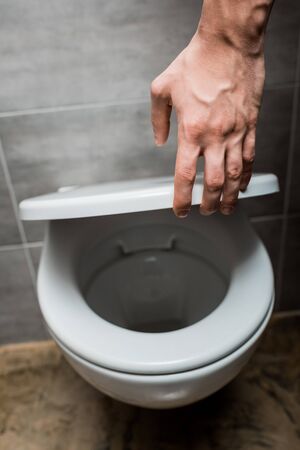 cropped view of man holding toilet lid in modern restroom with grey tileの写真素材