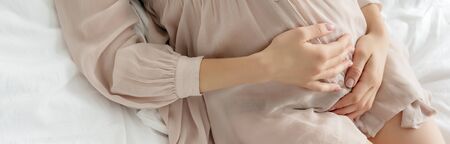 partial view of pregnant girl in nightie touching tummy while resting on bed, panoramic shot