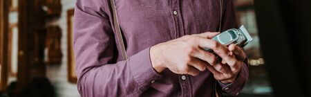 panoramic shot of barber holding trimmer in barbershop
