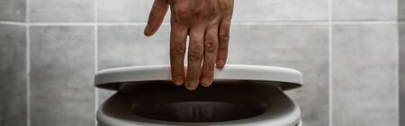 cropped view of man holding toilet lid in modern restroom with grey tile, panoramic shot