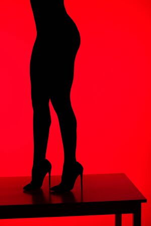 black silhouette of sexy elegant woman in heels posing on table, isolated on redの写真素材