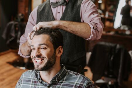 barber styling hair on cheerful bearded manの写真素材