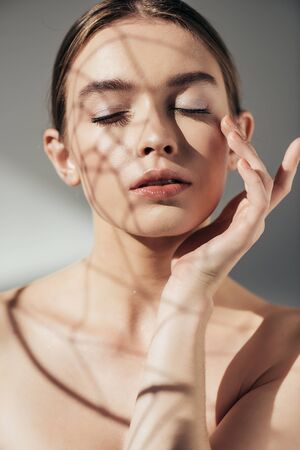 portrait of tender nude girl with closed eyes and shadows on face on grey