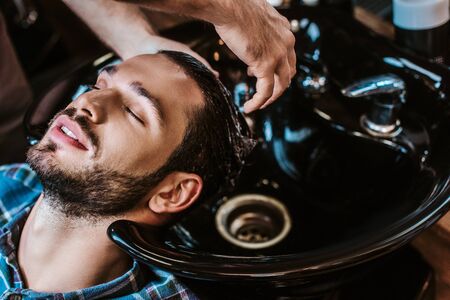 barber washing hair of bearded man in black sinkの写真素材