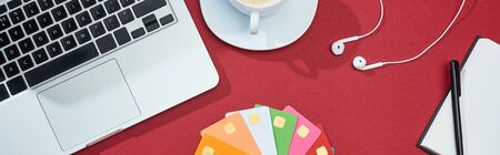 top view of multicolored empty credit cards on red background with laptop, earphones and coffee,...