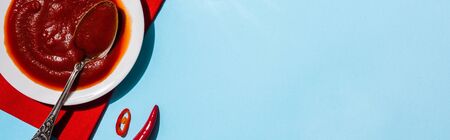Top view of plate with chili sauce with chili pepper on blue background, panoramic shot