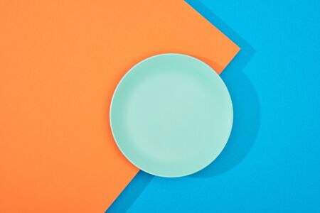 top view of empty plate on colorful blue and orange surfaceの写真素材