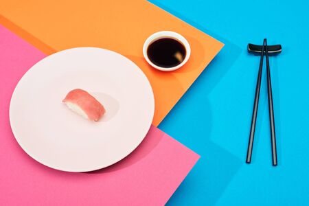 fresh nigiri with tuna near soy sauce and chopsticks on pink, blue, orange surfaceの写真素材