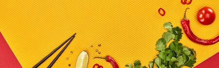 top view of chopsticks, lime, chili and coriander on red and yellow background, panoramic shot