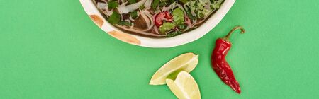 top view of pho in bowl near lime, chili on green background, panoramic shot