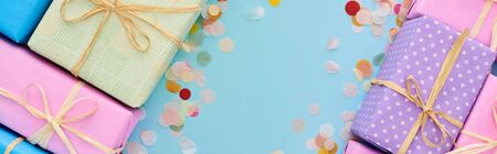 panoramic shot of wrapped gifts near colorful confetti on blueの写真素材
