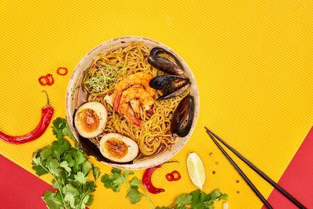top view of seafood ramen near fresh ingredients and chopsticks on yellow and red surface