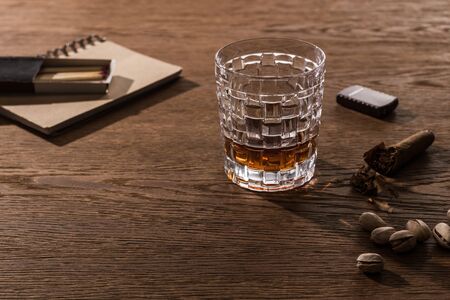 Brandy in glass with cigar, lighter and pistachios on wooden table