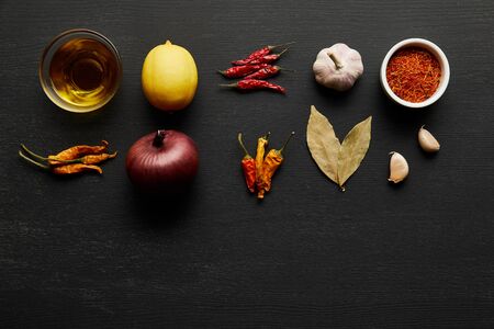Top view of spices, olive oil with onion and lemon on black wooden background