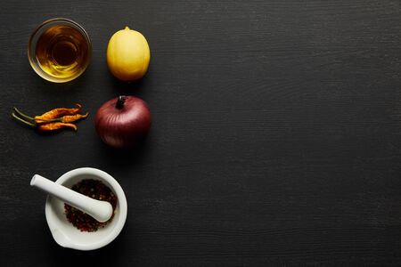 Top view of olive oil, chill peppers with lemon and onion on black wooden background