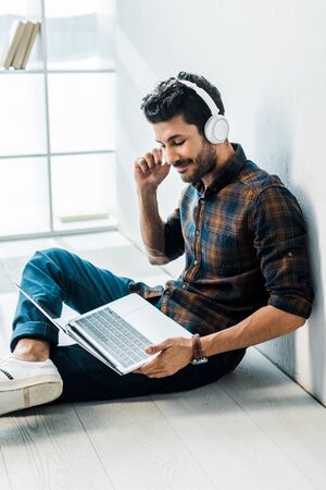 handsome and smiling bi-racial man with laptop listening musicの写真素材