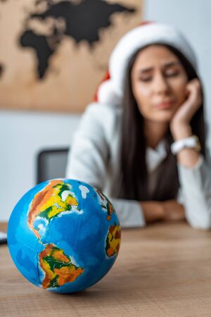 selective focus of pensive travel agent near globe at workplace