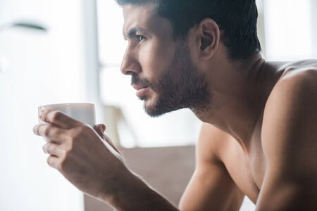 side view of handsome bi-racial man holding cup of coffee in morningの写真素材