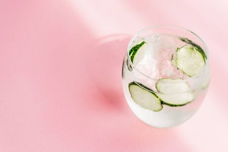 fresh lemonade with ice and cucumber slices on pink background with sunlightの写真素材