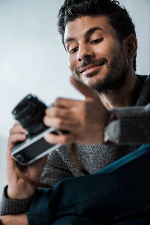 low angle view of handsome and smiling bi-racial man holding digital cameraの写真素材