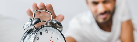 panoramic shot of bi-racial man holding alarm clock in morning