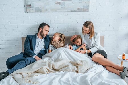 man and woman in formal wear lying in bed near diseased childrenの写真素材