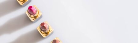 top view of assorted lipsticks in luxury tubes in line on white background, panoramic shot