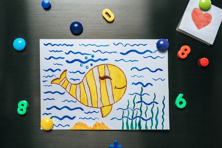 goldfish in ocean picture hanging on stainless steel fridge near heart and magnetsの写真素材
