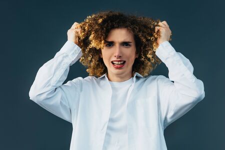 stressed curly teenager in total white outfit touching hair isolated on greenの写真素材