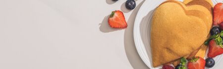 top view of heart shaped pancakes with tasty berries on plate on white background, panoramic shotの写真素材