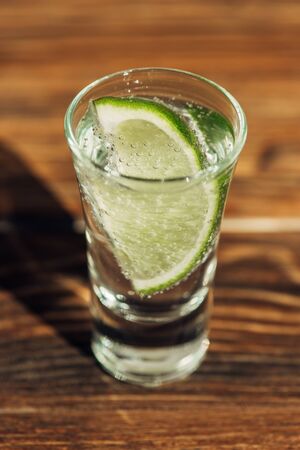 close up view of fresh tequila with lime on wooden surface in sunlightの写真素材