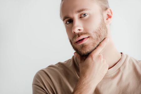 young handsome man in beige outfit touching face isolated on white
