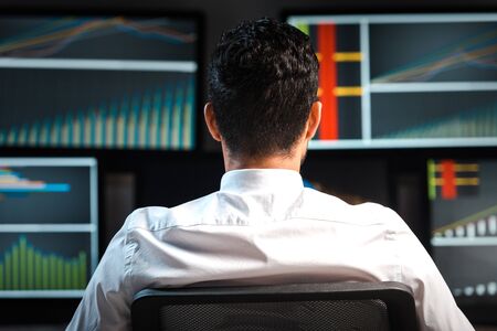 back view of bi-racial trader looking at computers with graphs