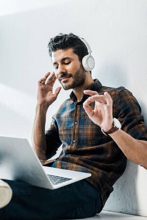 low angle view of handsome and smiling bi-racial man with laptop listening musicの写真素材