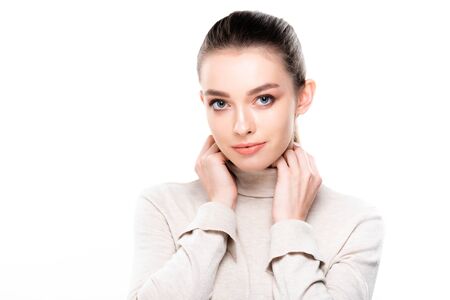 beautiful young woman with natural makeup holding hands near neck and looking at camera isolated on...