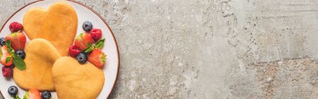 top view of heart shaped pancakes with berries on grey concrete surface, panoramic shot
