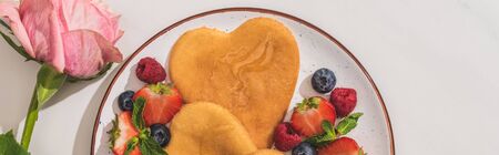 top view of delicious heart shaped pancakes with berries near rose on white background, panoramic shotの写真素材