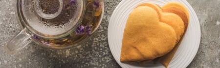top view of heart shaped pancakes near herbal tea in teapot on grey concrete surface, panoramic shot